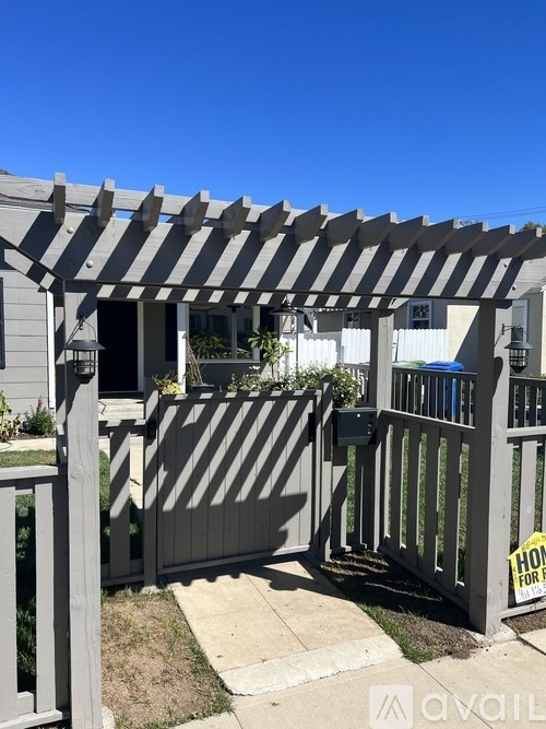 A house with a grey pergola and a fence with a "For Sale" sign.