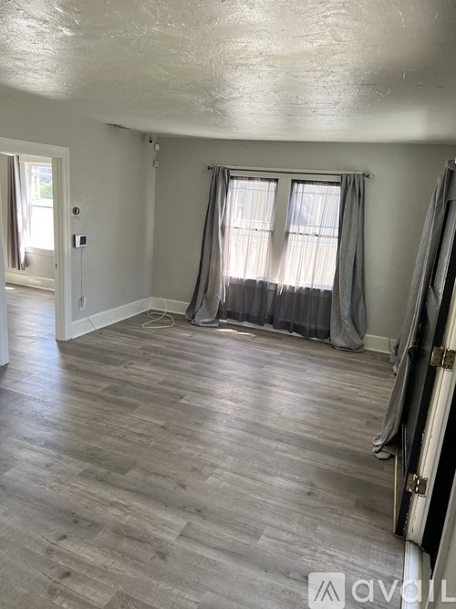 A room with wooden flooring and a window with curtains.