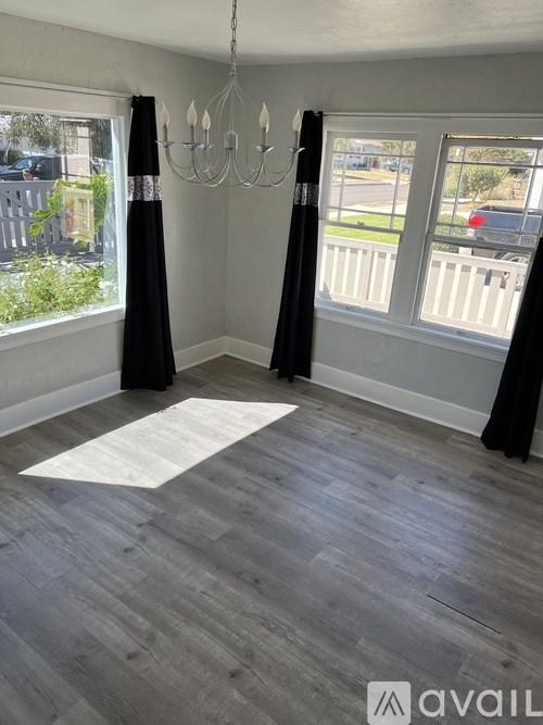 A room with a chandelier, curtains, and a wooden floor.