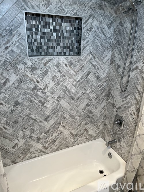 A white bathtub sits in a bathroom with a grey tiled wallpaper.