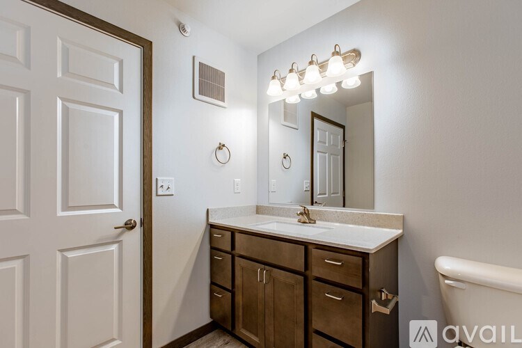 A bathroom with a white door, a vanity with a mirror and lights above it.
