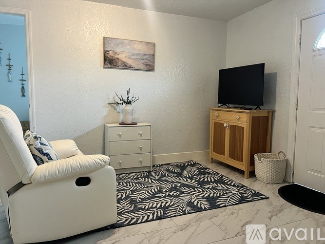 A living room with a white chair, a wooden cabinet, and a painting on the wall.
