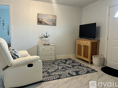A living room with a white chair, a wooden cabinet, and a painting on the wall.