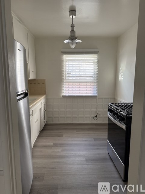 A kitchen with a refrigerator, oven, and a window with blinds.