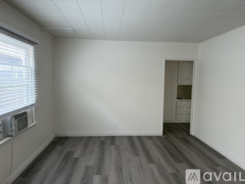 A room with white walls and wooden floors is shown with a doorway leading to another room.
