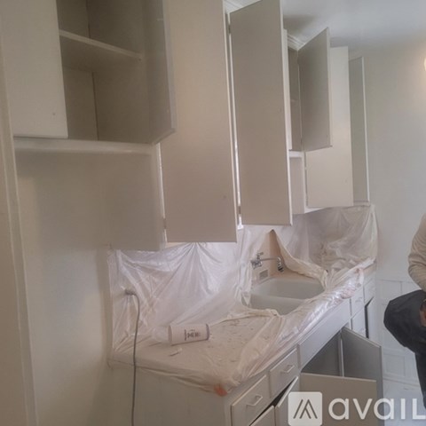 A person is standing in front of a kitchen with white cabinets and a sink.