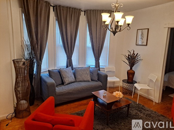 A living room with a grey couch, a red chair, and a chandelier.