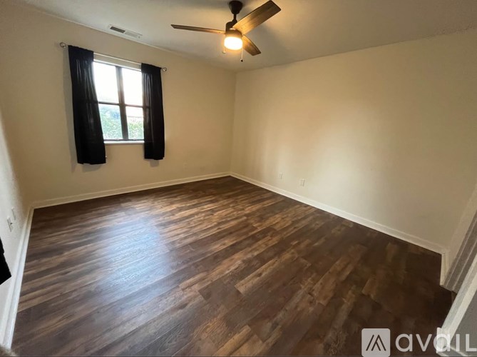 A room with wooden flooring and a window with black curtains.