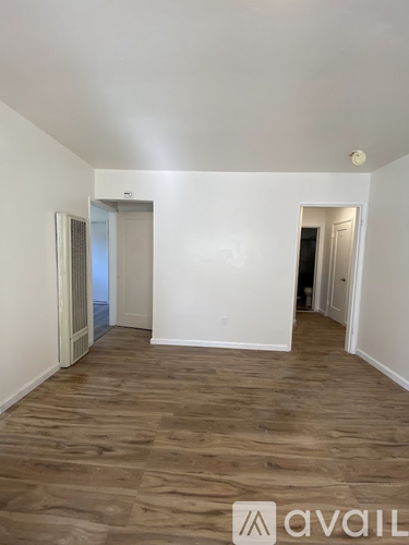 A room with wooden flooring and white walls, with a doorway leading to another room.