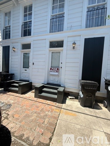 A white building with a black door and a "For Rent" sign.