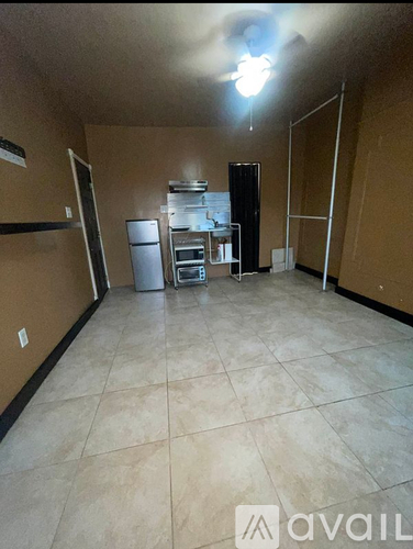 A room with a fan and a kitchenette in the background.