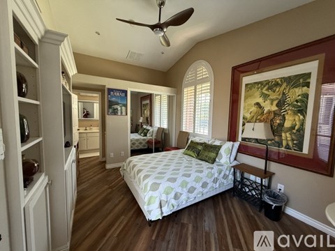 A bedroom with a bed, a ceiling fan, and a painting on the wall.