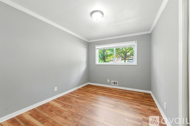 A room with wooden flooring and a window showing trees outside.