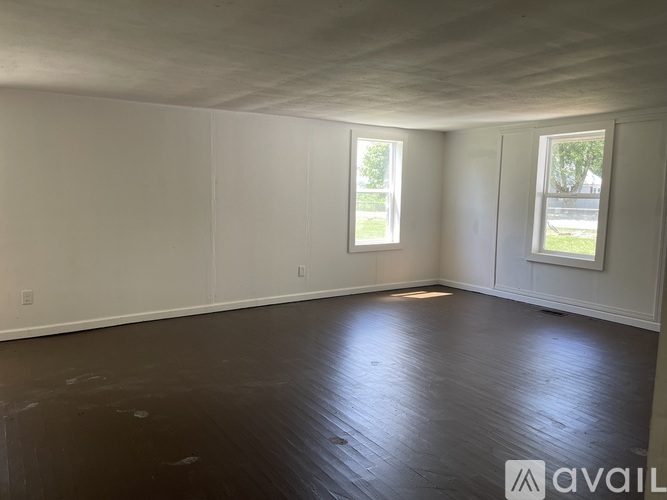 Empty room with two windows and wooden flooring.
