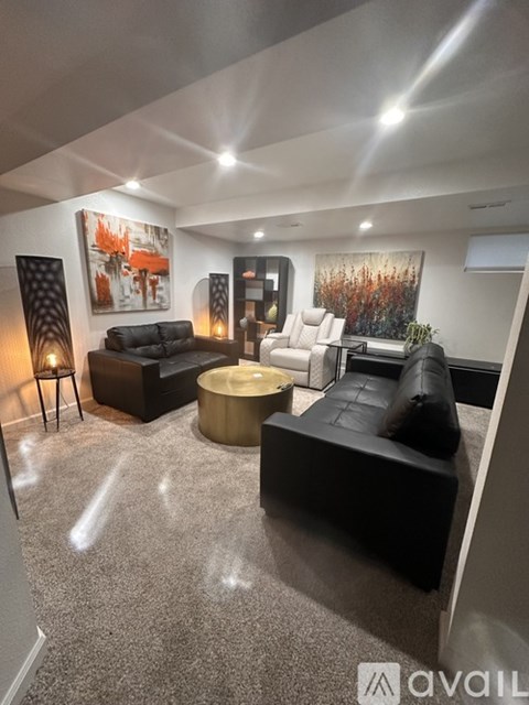 A living room with a black couch, a grey rug, and a painting on the wall.