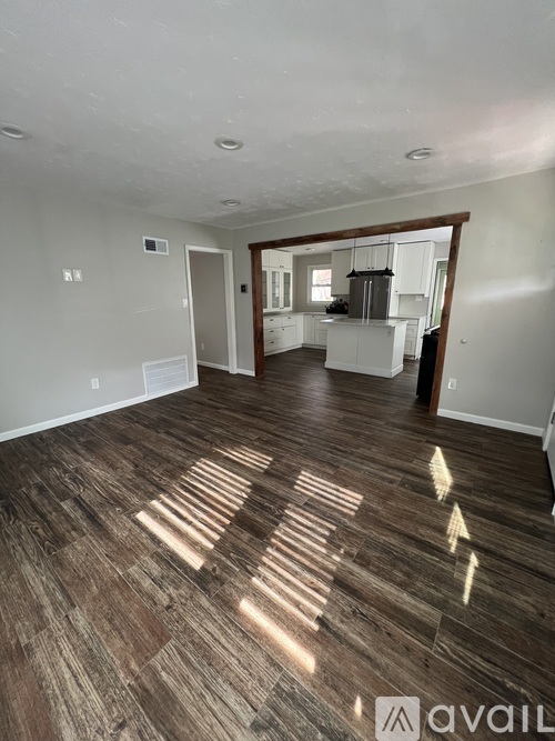 A room with wooden flooring and a kitchen area in the background.