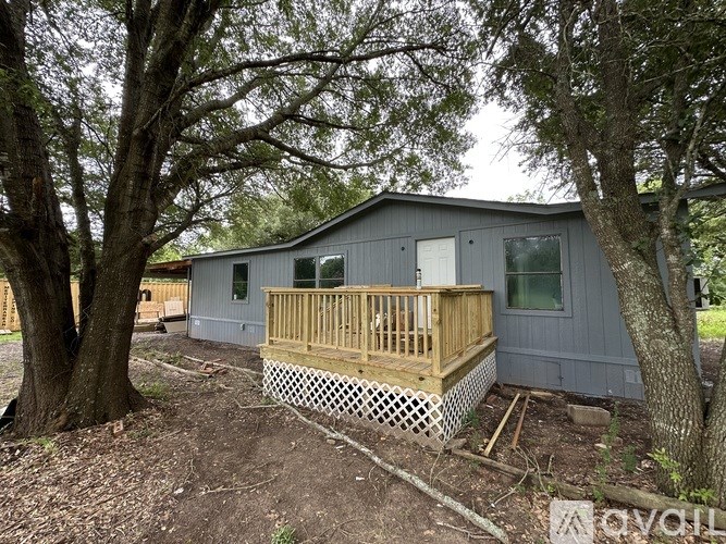 A grey house with a wooden deck surrounded by trees.