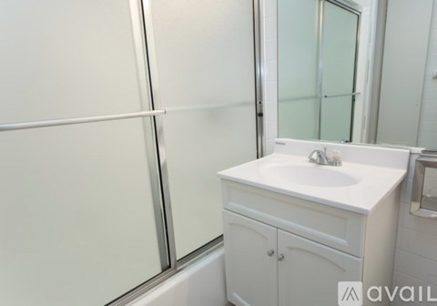 A white bathroom sink with a cabinet and a glass shower door.