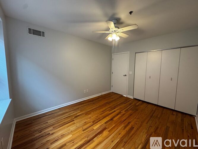 A room with wooden floors and white walls, featuring a ceiling fan and a window.
