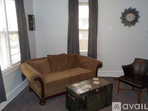 A brown couch sits in a living room with a clock on the wall.