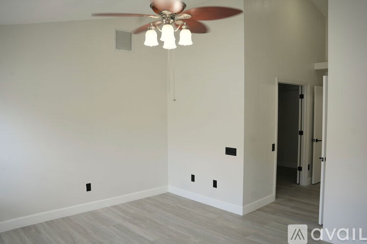 A room with a ceiling fan and light fixture, and a doorway leading to another room.