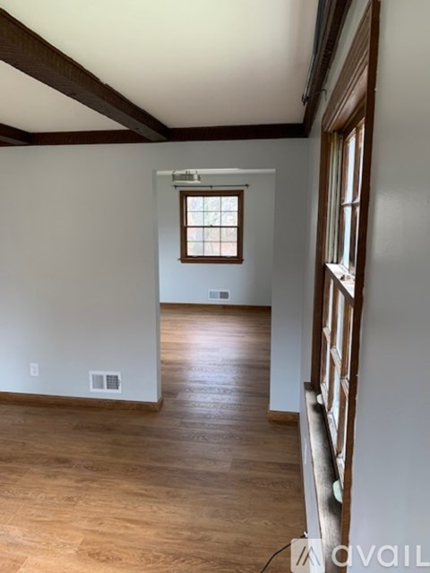 A room with wooden floors and white walls, with a window on the left wall.