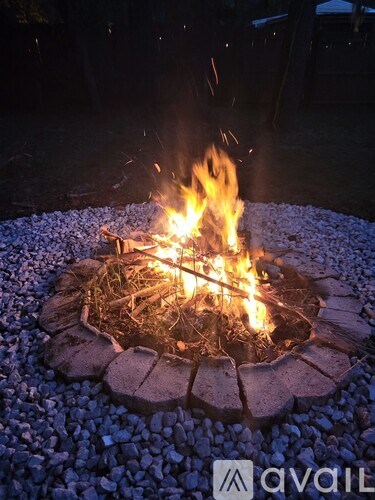 A fire burns in a fire pit on a gravel surface.