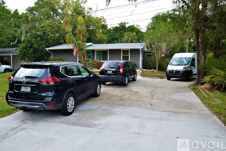 A black car is parked in a driveway with a white van and a grey house in the background.