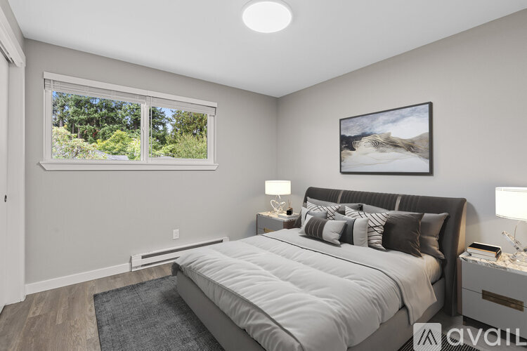 A bedroom with a large bed, a window with a view of trees, and a painting on the wall.