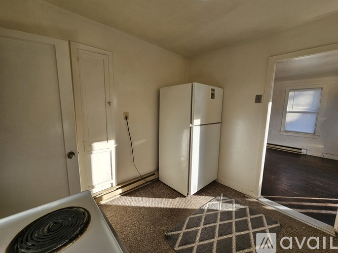 A room with a white refrigerator, a carpet, and a window.