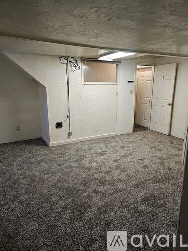 A carpeted room with a window and a door leading to another room.