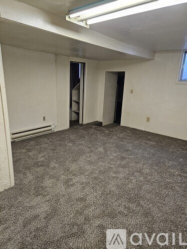 A room with carpeted floor and white walls, with a door on the left and a window on the right.
