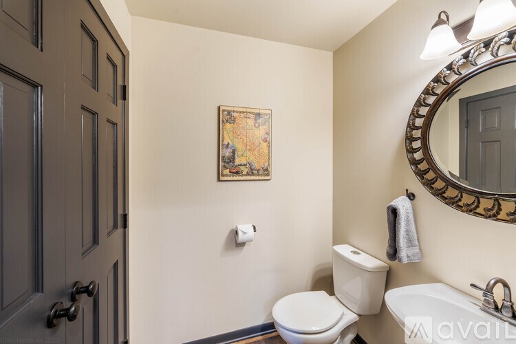A bathroom with a toilet, sink, mirror and a painting on the wall.
