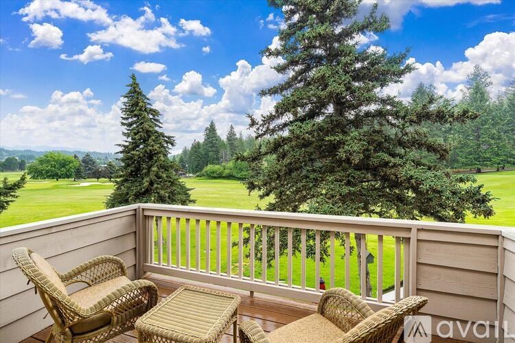 A balcony with wicker chairs and a table overlooks a grassy field.