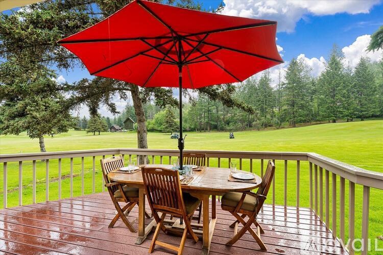 A red umbrella is on a wooden table with chairs on a wooden deck.