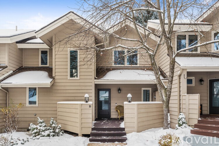 A beige house with a black door and a snow-covered ground.