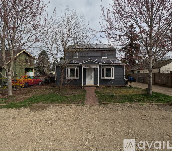 A house with a grey front yard and a red car parked in the driveway.