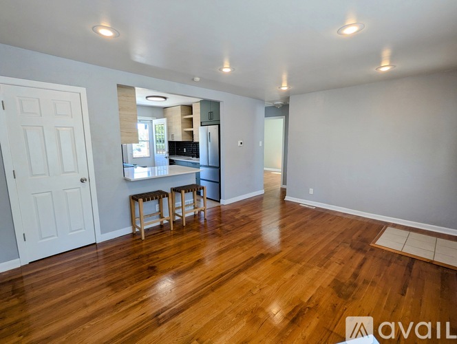 A living room with a white door and a kitchen in the background.