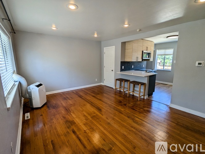 A room with wooden floors and a kitchen area in the background.