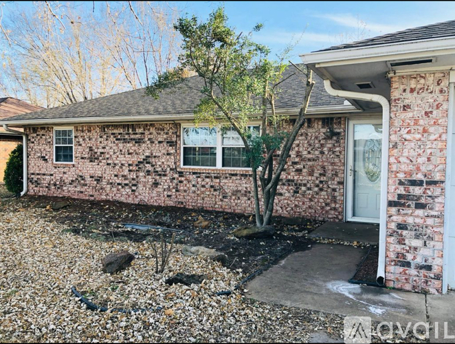 A house with a tree in front and a gravel area in front of it.