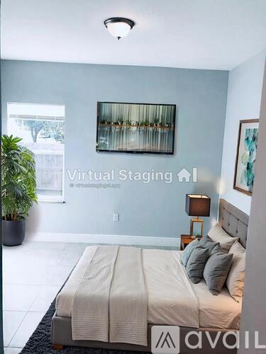 A bedroom with a bed, a plant, and a painting on the wall.