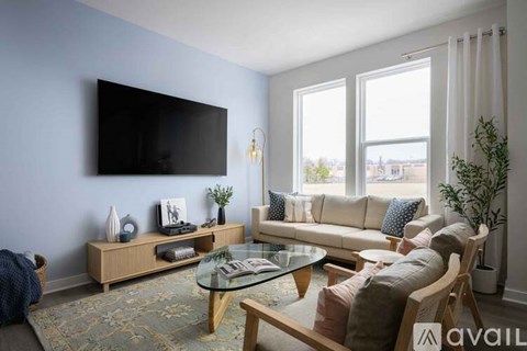 A living room with a flat screen TV mounted on the wall, a glass coffee table, and a sofa with cushions.