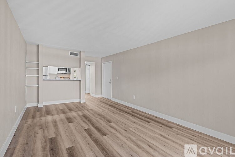 A room with wooden flooring and white walls, with a white door and a window with blinds.