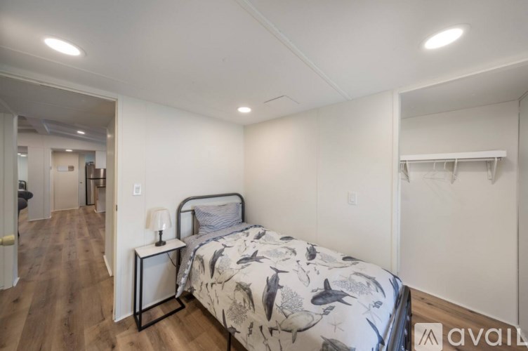 A bedroom with a bed, nightstand, and a wall-mounted shelf.