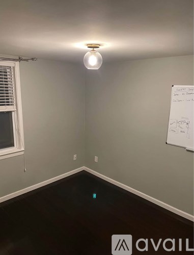 A whiteboard with writing on it is on a wall in a room with a window and a light on.