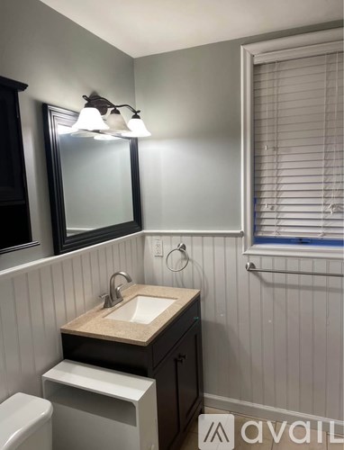 A bathroom with a sink, toilet, mirror, and window.