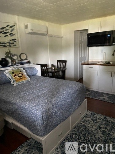 A bedroom with a bed, chair, and a microwave in the kitchen.