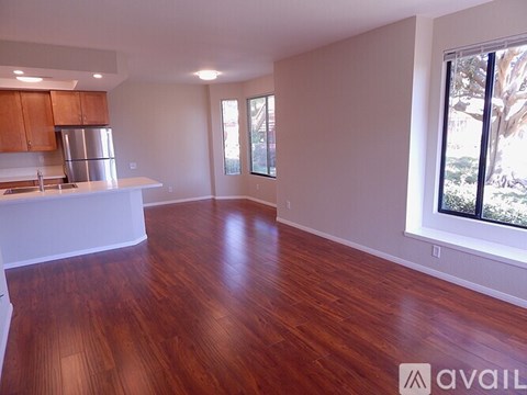 A spacious room with wooden floors and a kitchen area with a refrigerator and cabinets.
