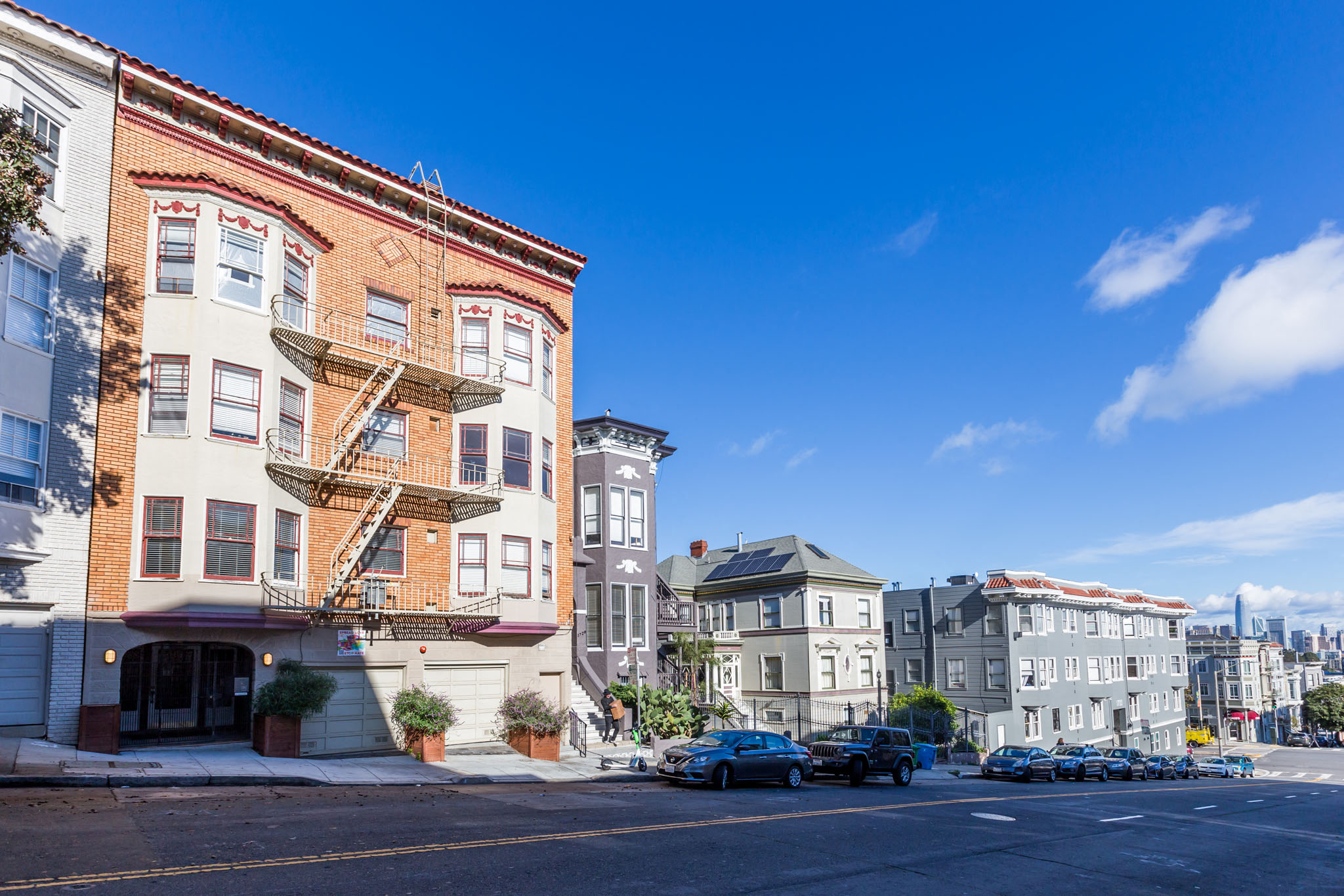 A street view of a residential area with buildings and parked cars.