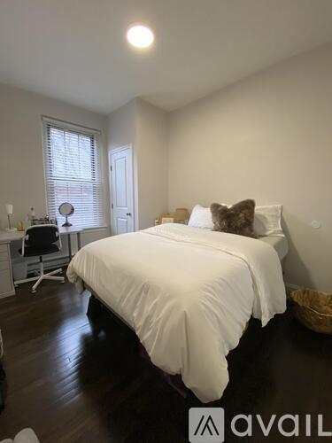 A bedroom with a white bed and a window with blinds.